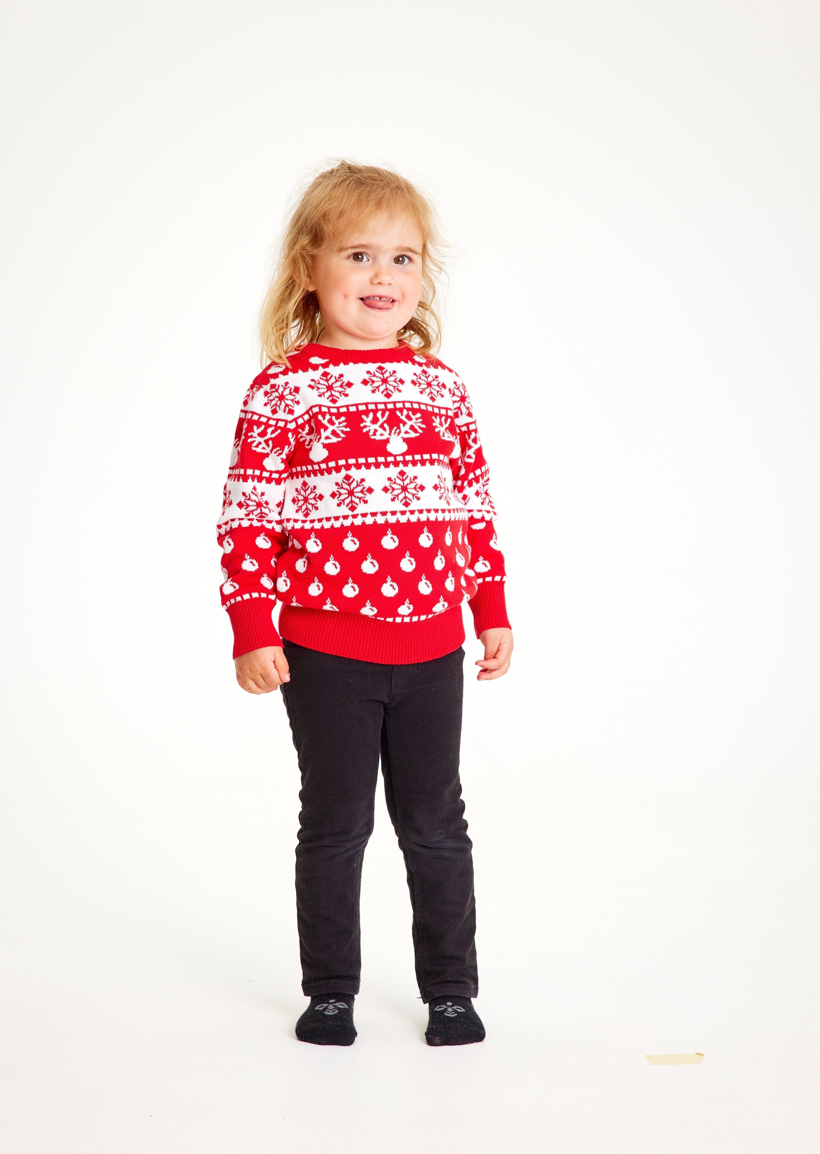 Un enfant portant un pull de Noël rouge et blanc avec des flocons de neige et un motif.